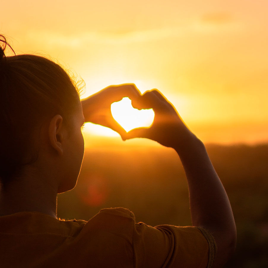 Imagen chica de espaldas con puesta de sol haciendo un corazón con sus manos
