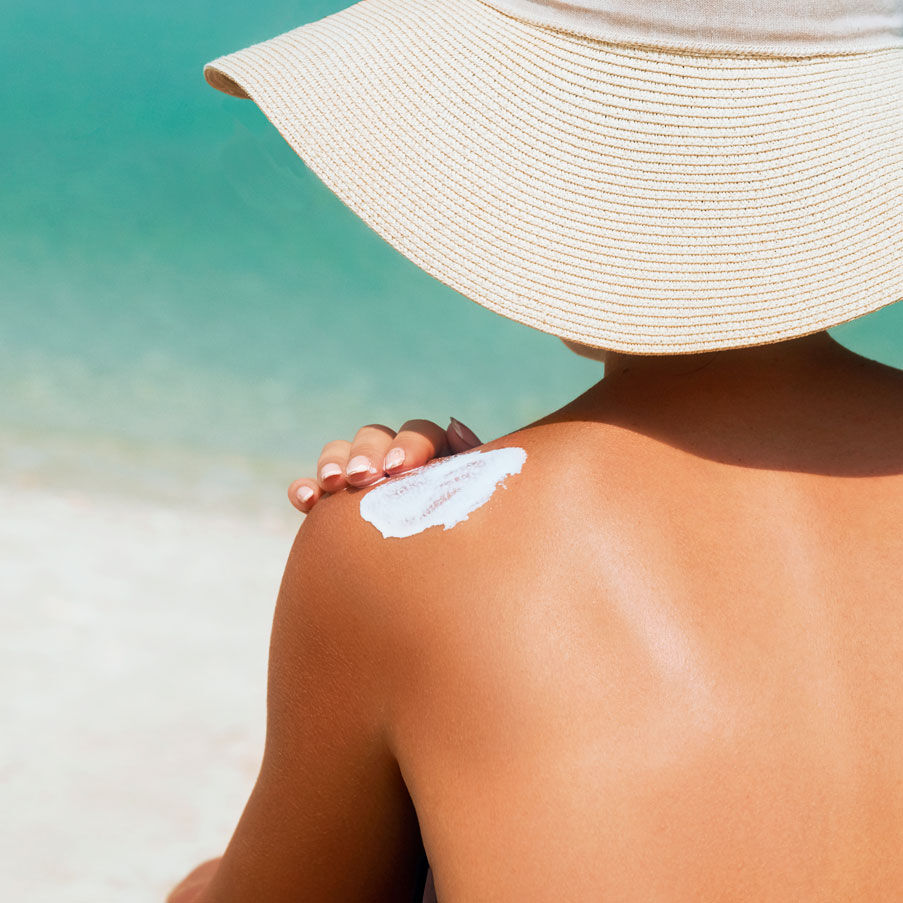 Imagen chica nen la playa de espaldas con sombrero y crema solar en el hombro