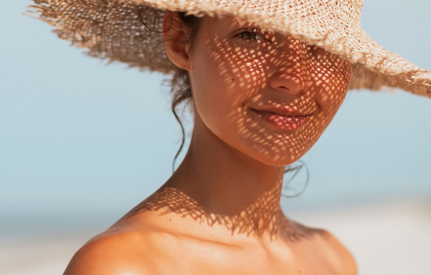 Imagen chica playa con sombrero dándole el sol