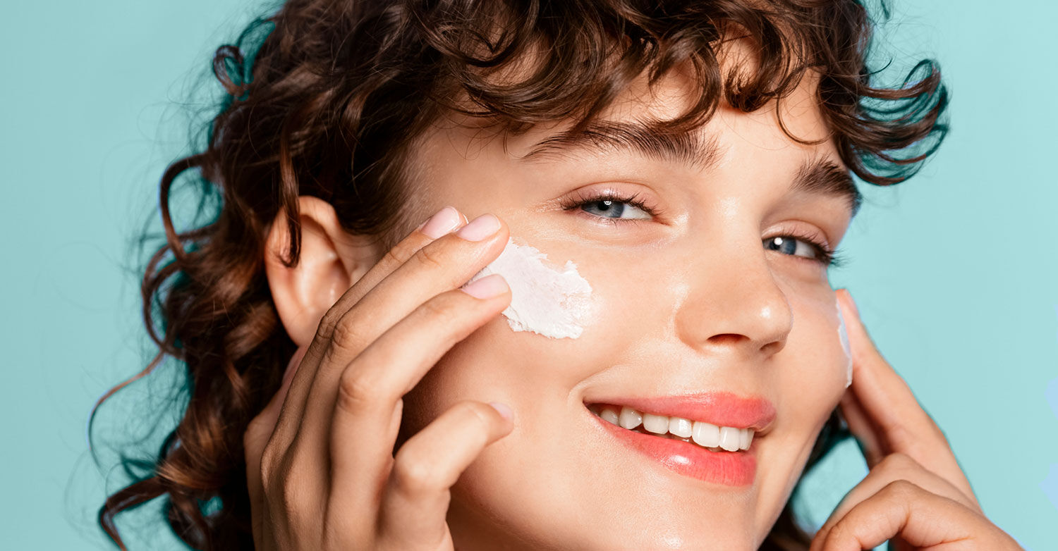 Imagen chica sonriente aplicándose crema en la cara