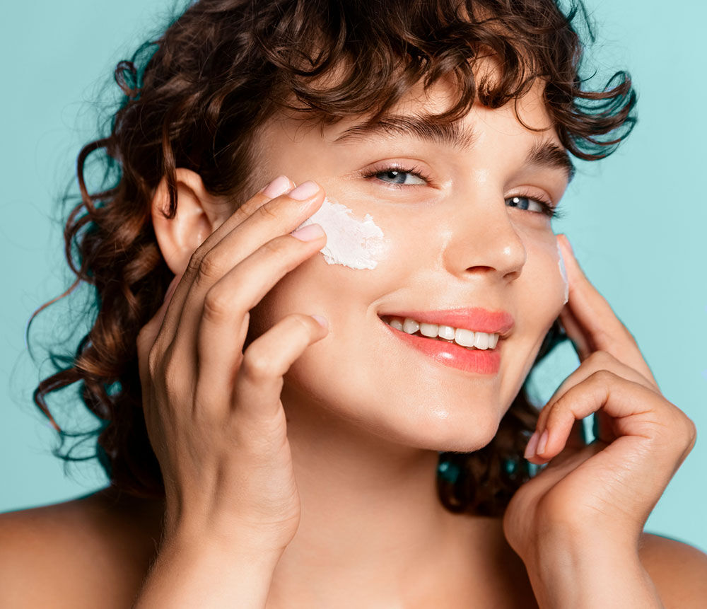 Imagen chica sonriente aplicándose crema en la cara